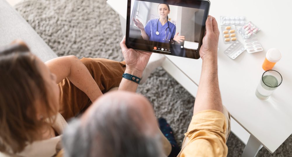 Using eHealth and telemedicine services at home. Senior couple sitting on sofa with digital tablet, having video call with online doctor and getting professional health consultation